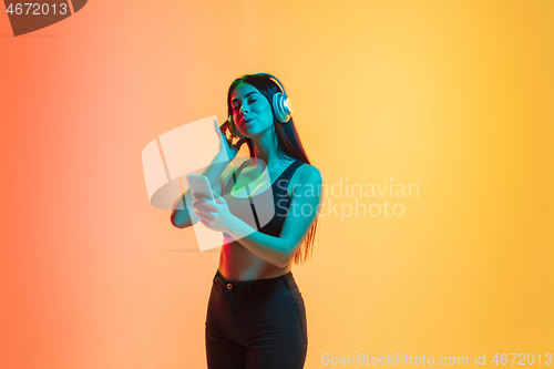 Image of Young woman\'s portrait on yellow-orange studio background in neon light