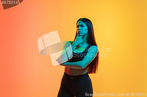 Image of Young woman\'s portrait on yellow-orange studio background in neon light