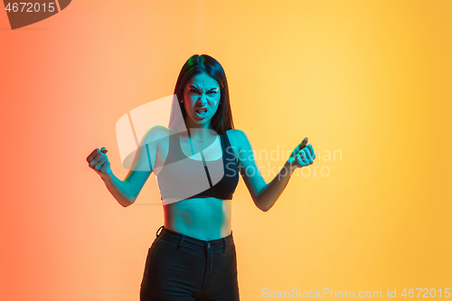 Image of Young woman\'s portrait on yellow-orange studio background in neon light