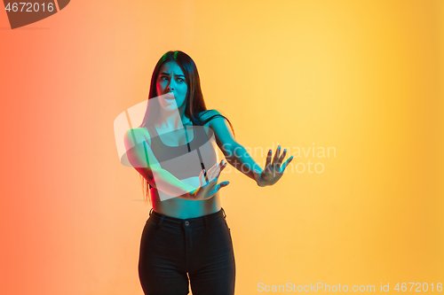 Image of Young woman\'s portrait on yellow-orange studio background in neon light