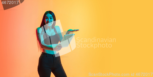 Image of Young woman\'s portrait on yellow-orange studio background in neon light