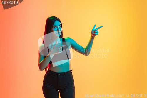 Image of Young woman\'s portrait on yellow-orange studio background in neon light