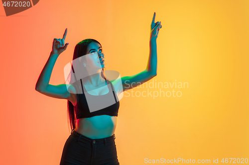 Image of Young woman\'s portrait on yellow-orange studio background in neon light