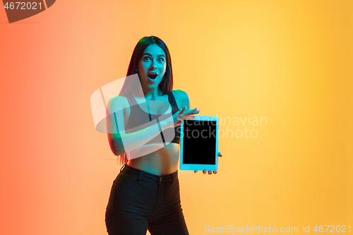 Image of Young woman\'s portrait on yellow-orange studio background in neon light