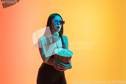 Image of Young woman\'s portrait on yellow-orange studio background in neon light