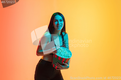 Image of Young woman\'s portrait on yellow-orange studio background in neon light