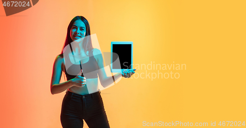 Image of Young woman\'s portrait on yellow-orange studio background in neon light