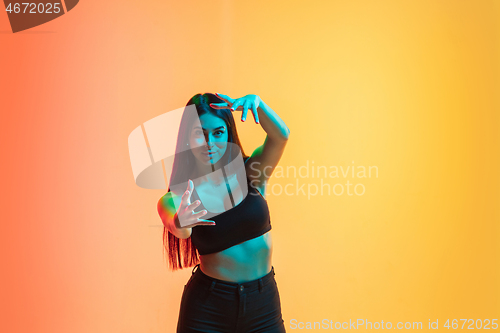 Image of Young woman\'s portrait on yellow-orange studio background in neon light