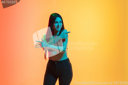 Image of Young woman\'s portrait on yellow-orange studio background in neon light