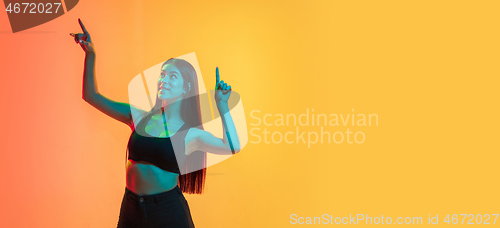 Image of Young woman\'s portrait on yellow-orange studio background in neon light