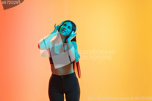 Image of Young woman\'s portrait on yellow-orange studio background in neon light