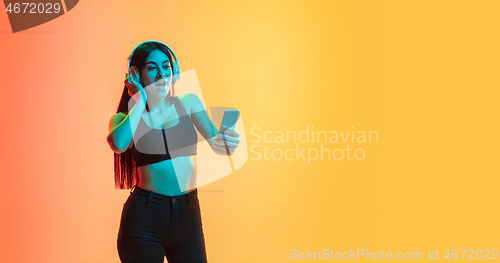 Image of Young woman\'s portrait on yellow-orange studio background in neon light