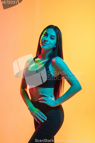 Image of Young woman\'s portrait on yellow-orange studio background in neon light