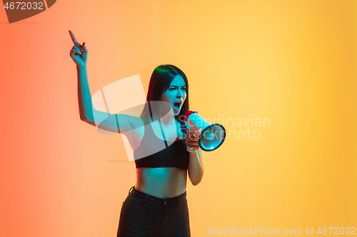 Image of Young woman\'s portrait on yellow-orange studio background in neon light