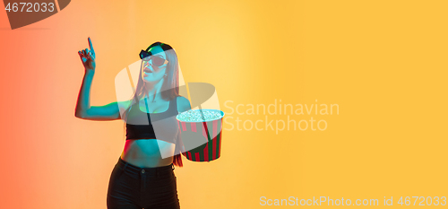 Image of Young woman\'s portrait on yellow-orange studio background in neon light