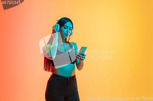 Image of Young woman\'s portrait on yellow-orange studio background in neon light