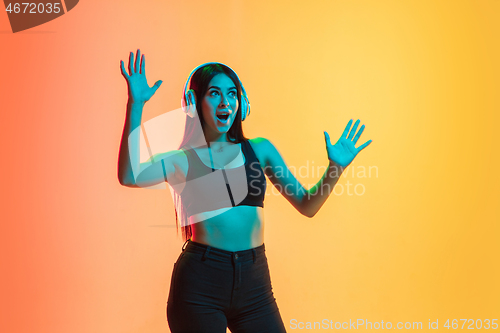 Image of Young woman\'s portrait on yellow-orange studio background in neon light