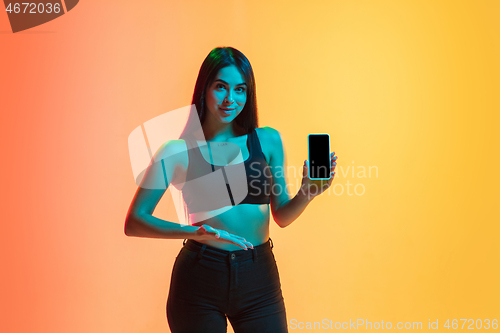 Image of Young woman\'s portrait on yellow-orange studio background in neon light