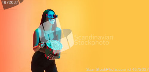 Image of Young woman\'s portrait on yellow-orange studio background in neon light