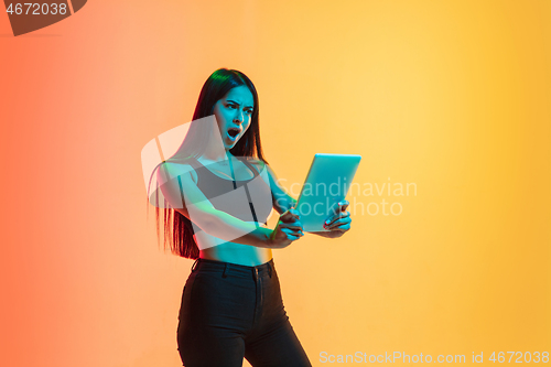 Image of Young woman\'s portrait on yellow-orange studio background in neon light