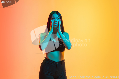 Image of Young woman\'s portrait on yellow-orange studio background in neon light