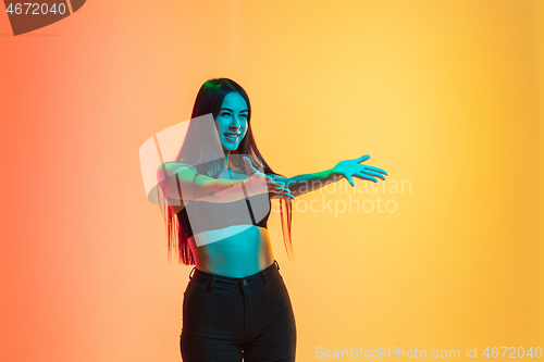 Image of Young woman\'s portrait on yellow-orange studio background in neon light