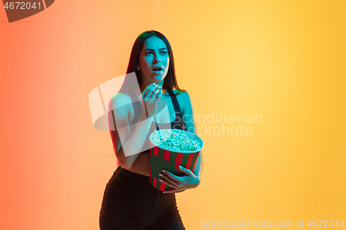 Image of Young woman\'s portrait on yellow-orange studio background in neon light