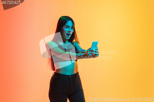 Image of Young woman\'s portrait on yellow-orange studio background in neon light