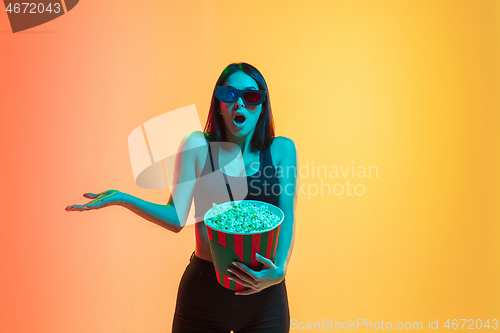 Image of Young woman\'s portrait on yellow-orange studio background in neon light