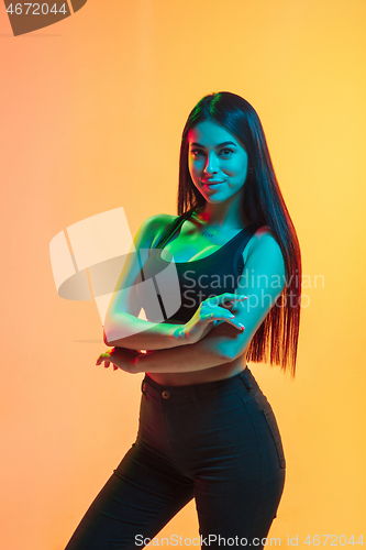 Image of Young woman\'s portrait on yellow-orange studio background in neon light