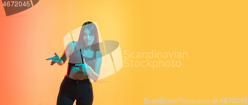 Image of Young woman\'s portrait on yellow-orange studio background in neon light