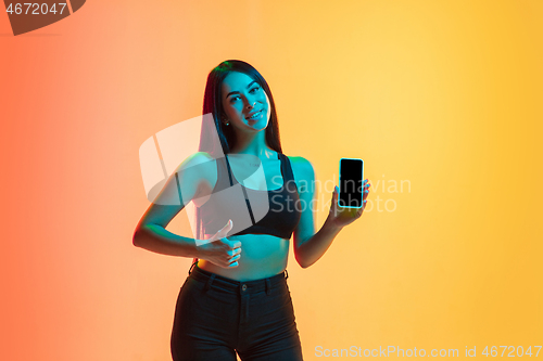 Image of Young woman\'s portrait on yellow-orange studio background in neon light