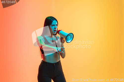 Image of Young woman\'s portrait on yellow-orange studio background in neon light