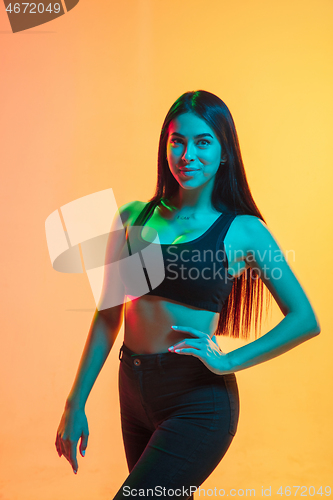 Image of Young woman\'s portrait on yellow-orange studio background in neon light