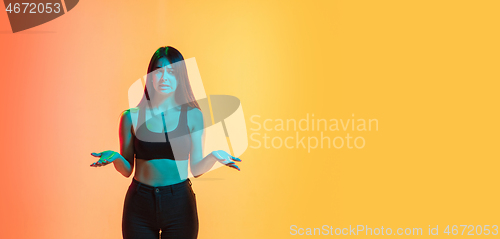 Image of Young woman\'s portrait on yellow-orange studio background in neon light