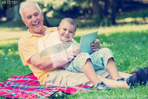 Image of grandfather and child in park using tablet