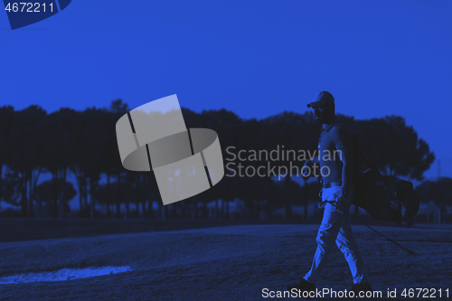 Image of golfer  walking and carrying golf  bag at beautiful sunset