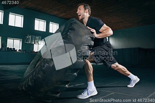 Image of Shirtless man flipping heavy tire at gym