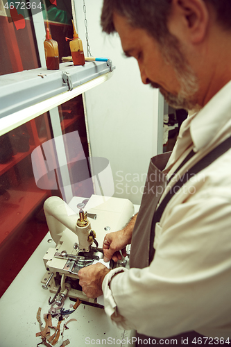 Image of Sewing process of the leather belt. old Man\'s hands behind sewing.