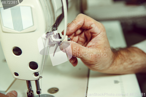 Image of Sewing process of the leather belt. old Man\'s hands behind sewing.