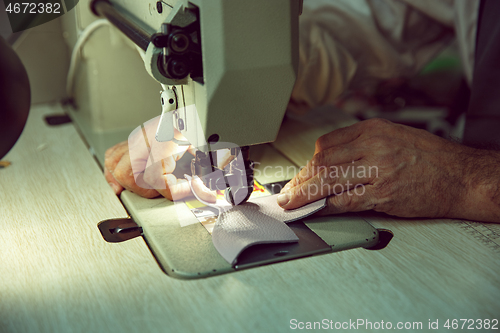 Image of Sewing process of the leather belt. old Man\'s hands behind sewing.