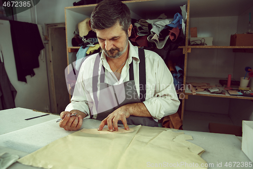 Image of Closeup of tailors table with male hands tracing fabric making pattern for clothes