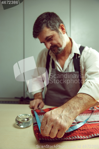 Image of Closeup of tailors table with male hands tracing fabric making pattern for clothes