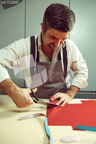 Image of Closeup of tailors table with male hands tracing fabric making pattern for clothes