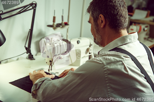 Image of Sewing process of the leather belt. old Man\'s hands behind sewing.