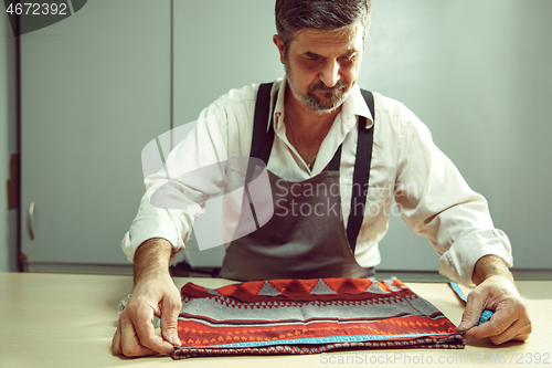 Image of Closeup of tailors table with male hands tracing fabric making pattern for clothes