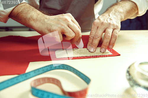 Image of Closeup of tailors table with male hands tracing fabric making pattern for clothes