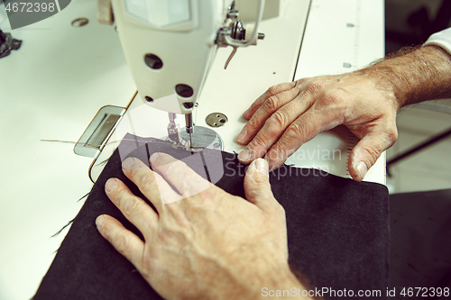 Image of Sewing process of the leather belt. old Man\'s hands behind sewing.