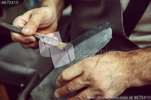 Image of Shoemaker makes shoes for men.He smears special liquid with a brush.