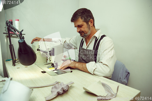 Image of Sewing process of the leather belt. old Man\'s hands behind sewing.